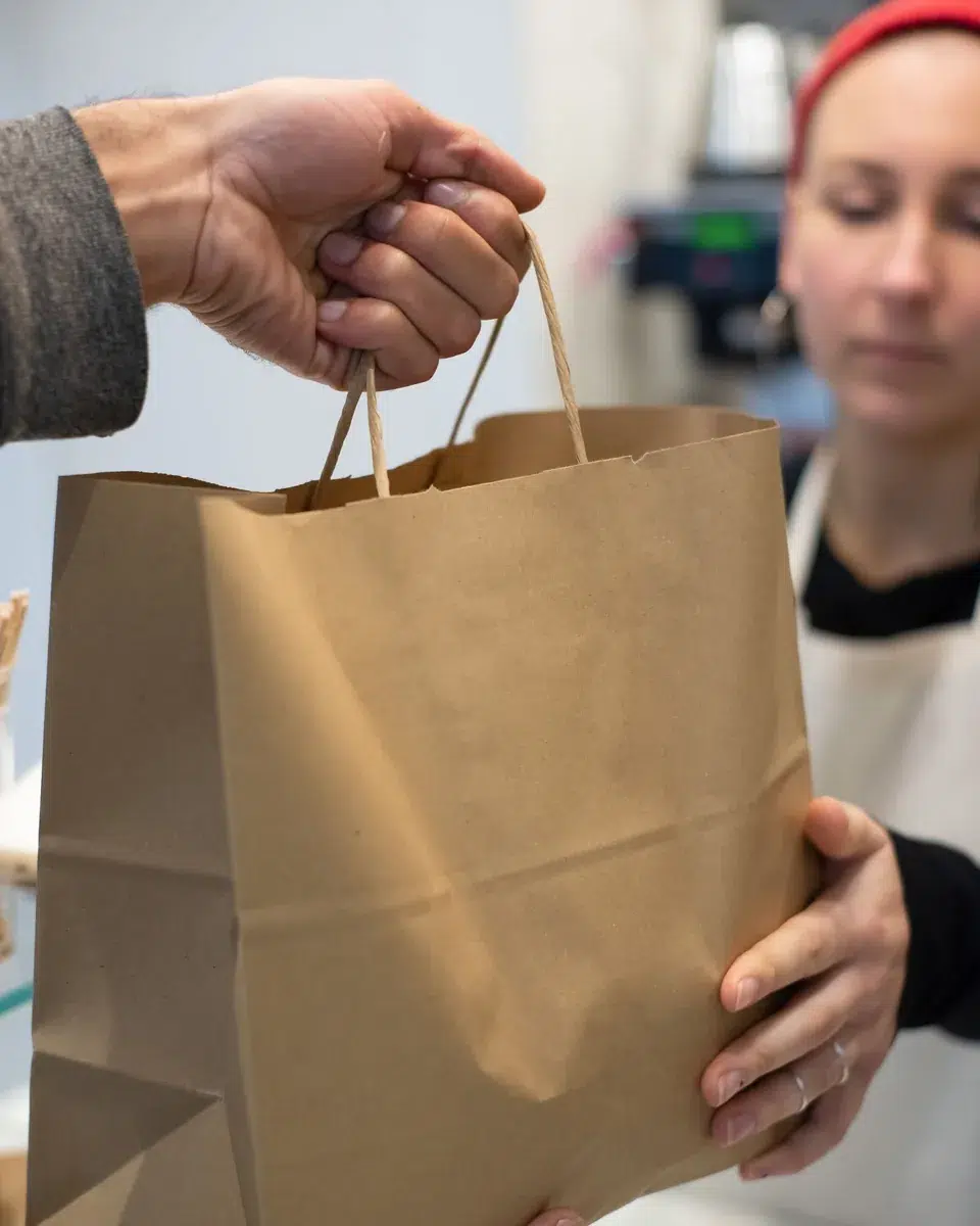 Una empleada entrega una bolsa de papel con un pedido para llevar a un cliente