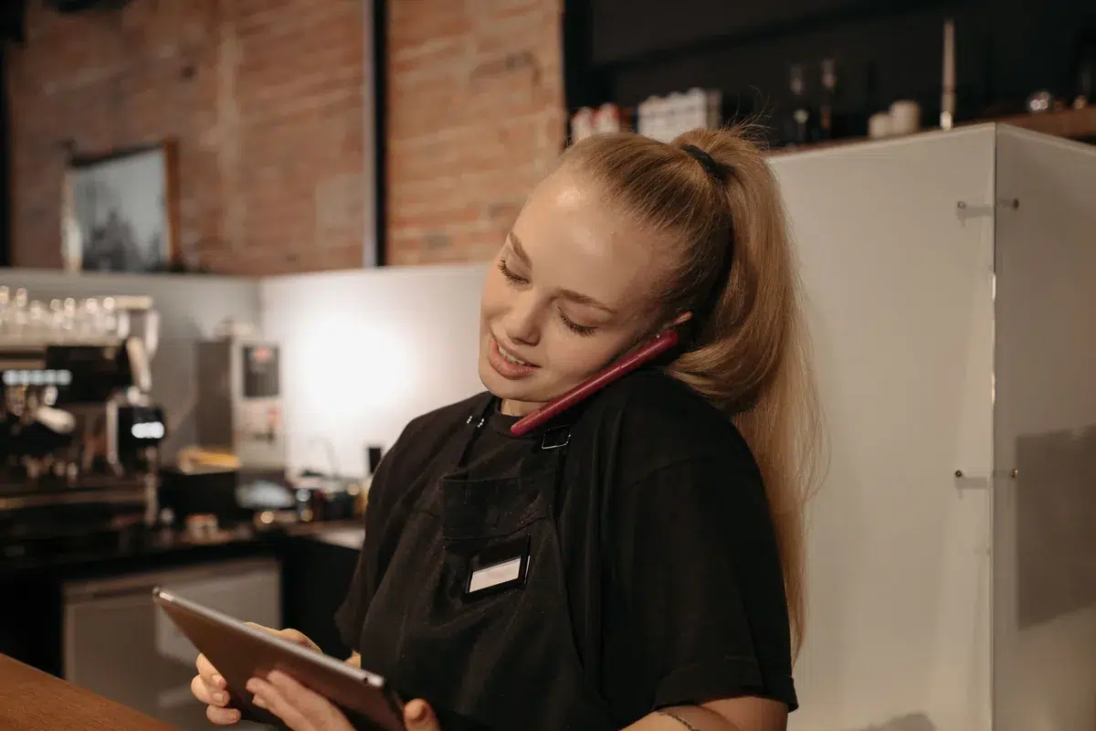 Una empleada de un restaurante toma un pedido por teléfono mientras revisa la tableta en el mostrador